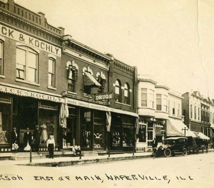 Oswald's Pharmacy exterior in 1925. Jefferson street in downtown Naperville is the setting, showing Oswald's wedged between two other business. An antique car is parked out front.
