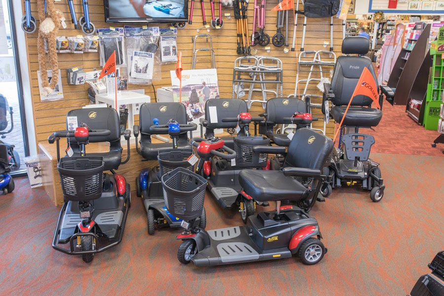 Renting or Purchasing Scooters featured image. The front section of Oswald's Medical Equipment Showroom, 7 mobility scooters can be seen displayed against a wall filled with scooter accessories.