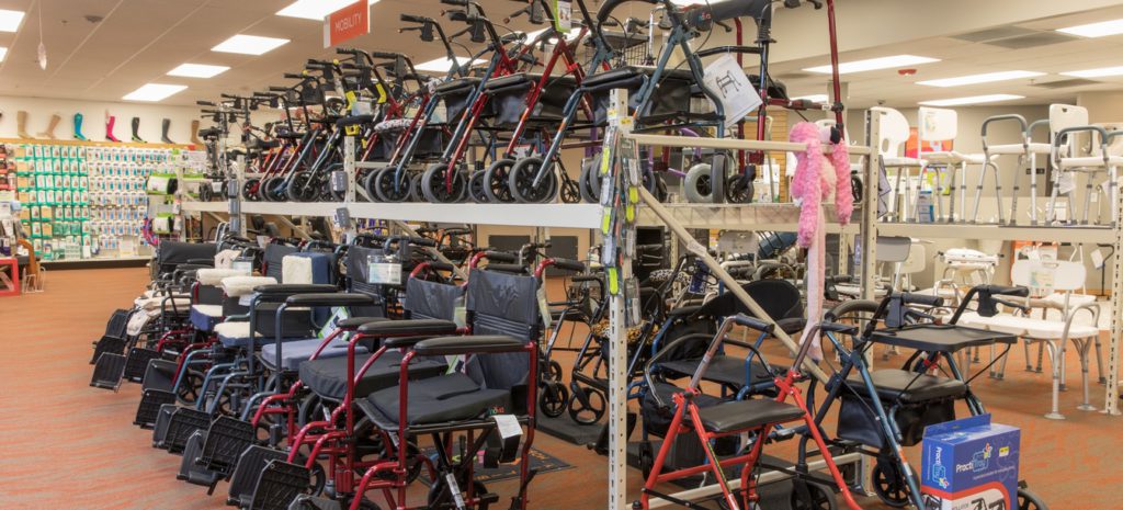 Medical Equipment Landing Page. A shot of the Oswald's Pharmacy Medical Equipment showroom. A large 2 tier rack with dozens of wheelchairs and walkers stacked on it. Red carpet.