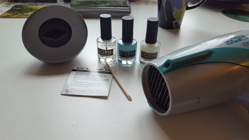 SOPHi Blog inset image. .5oz botles of SOPHi primer, shiner and blue polish on a table, next to a blow dryer and SOPHi polish removal stick. All the essentials for SOPHi polish!