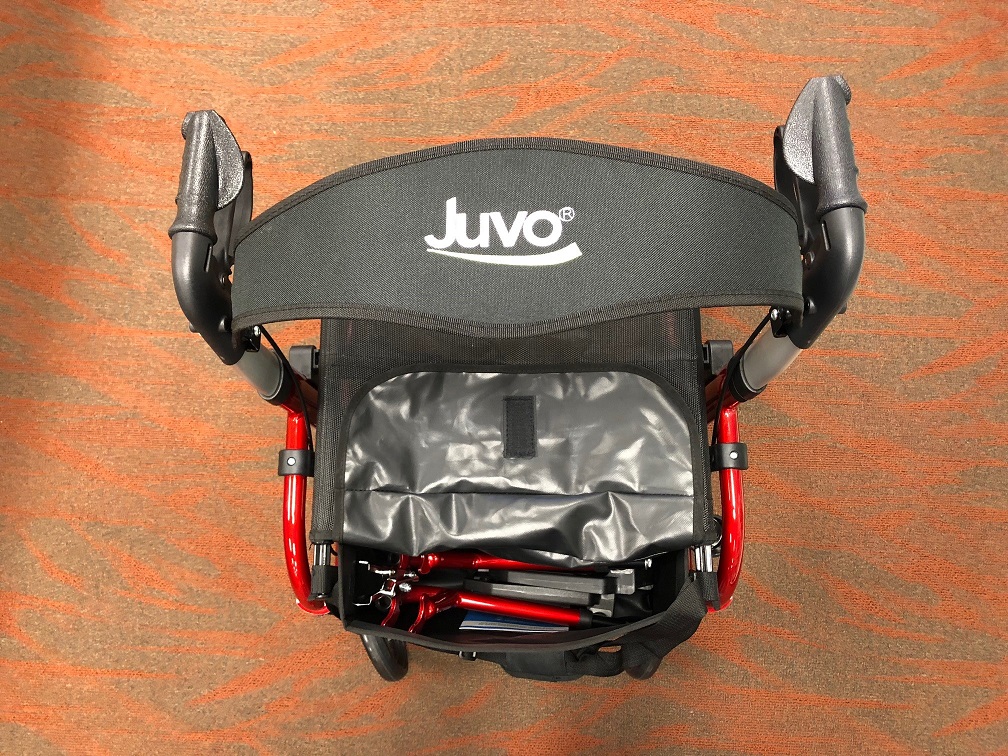 Overhead shot of the Juvo Rollator-Transport Chair to show the open accessory bag. Both of the transport chair footrests are in the accessory bag, with plenty of room to spare. The Juvo logo is visible on the backrest, which is flipped up for better visibility of the accessory bag.