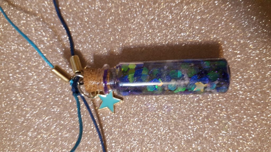 Alecia's finished Creativity for Kids Charm. A Glass vial filled with glitter and colored gems. Corked, with a small star charm.