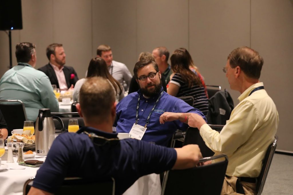 Oswald's Manager Alex Anderson sitting at a conference table at Medtrade 2018, surrounded by other attendees.