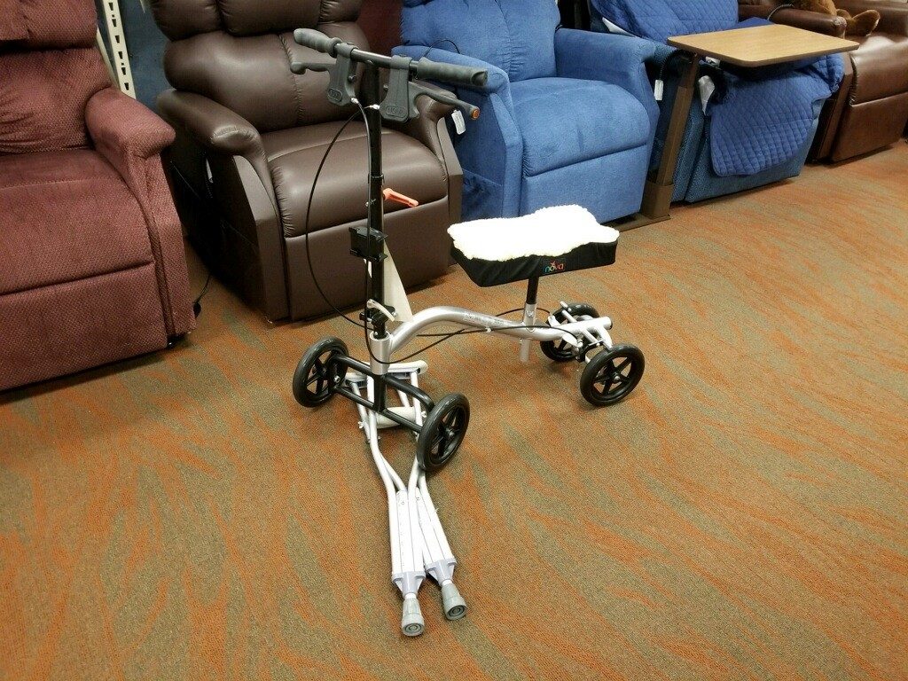 Image of a knee scooter running over a pair of crutches on the Oswald's Medical Equipment Showroom floor. A row of power lift recliners is seen in the background.
