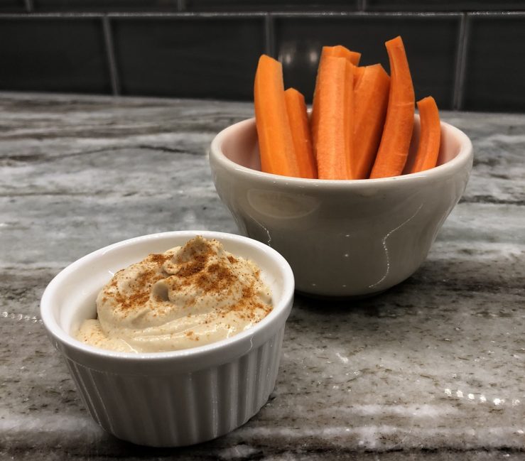 A bowl of carrots next to a bowl of hummus, prepared by Allison.