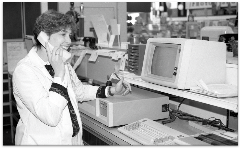 Oswald's Pharmacist Mary Loggins in the 1980s. Photo of Mary working on the phone at the Oswald's Pharmacy counter in the 1980s.