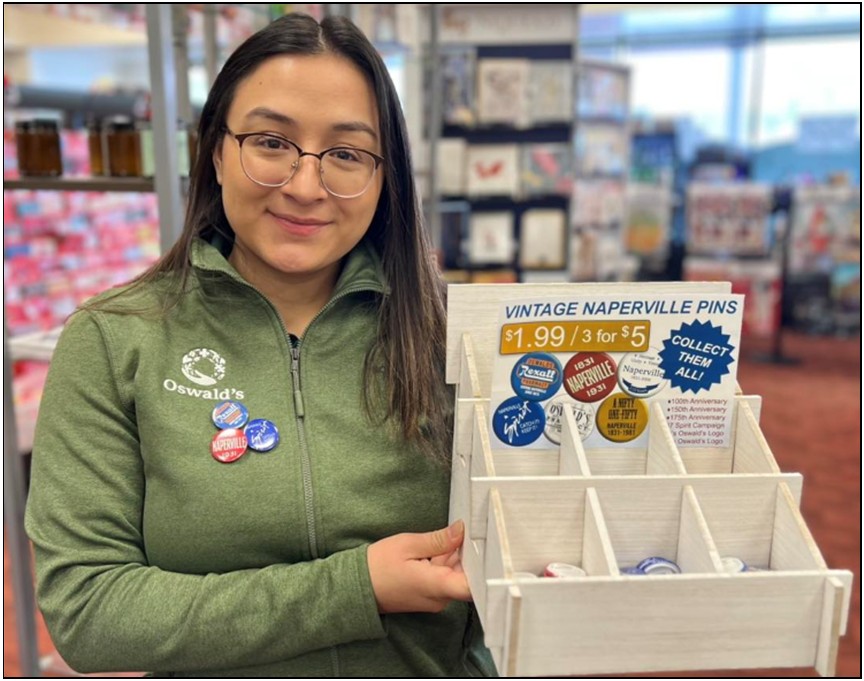 An image of Oswald's Employee Jackie holding up a display of the new vintage 1.25" Naperville Pins