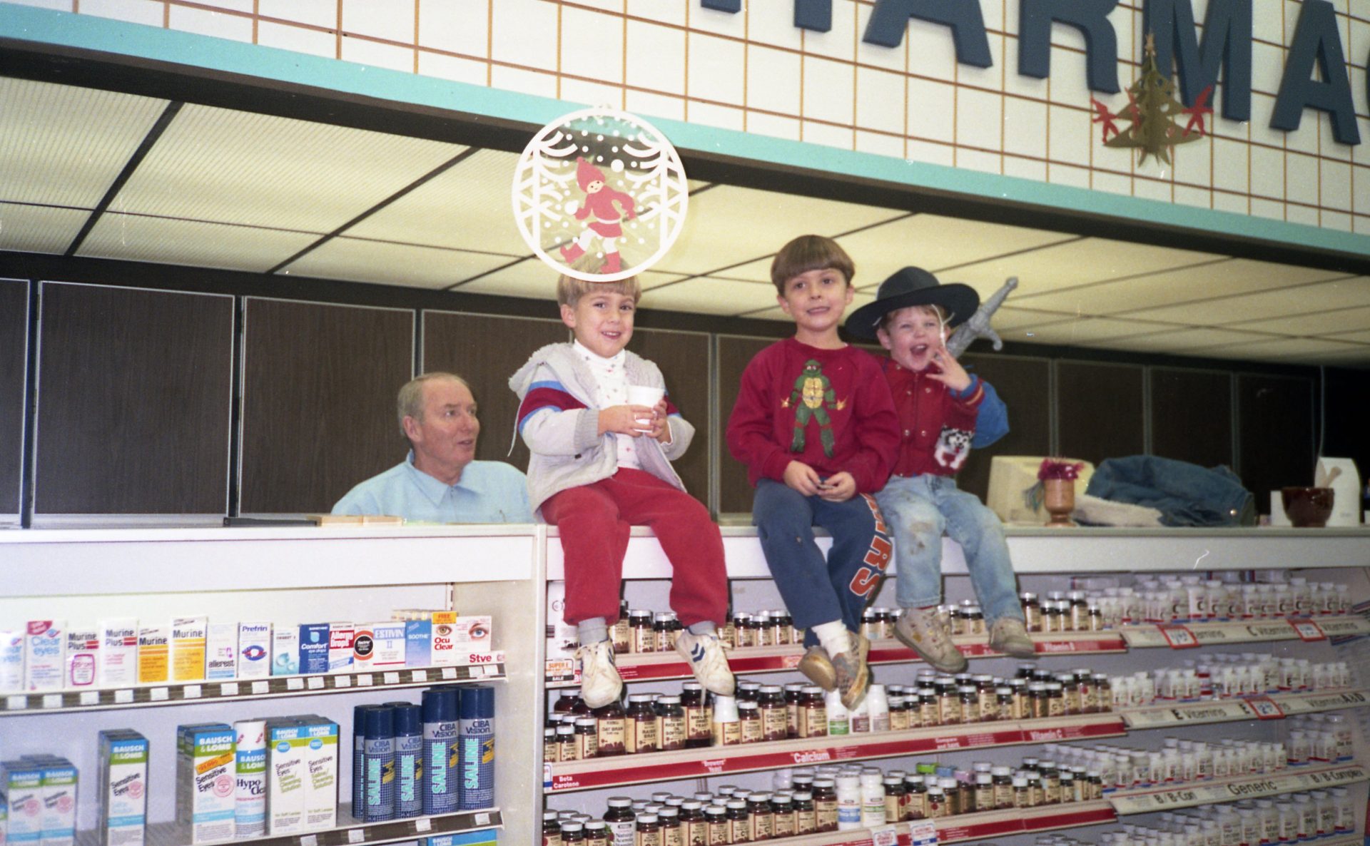 Fourth-generation owner Bob Anderson stands behind the Oswald’s Pharmacy counter in 1991 with his grandchildren, including future sixth-generation owner Alex Anderson, along with Wil and Max, sitting on the shelf above.
